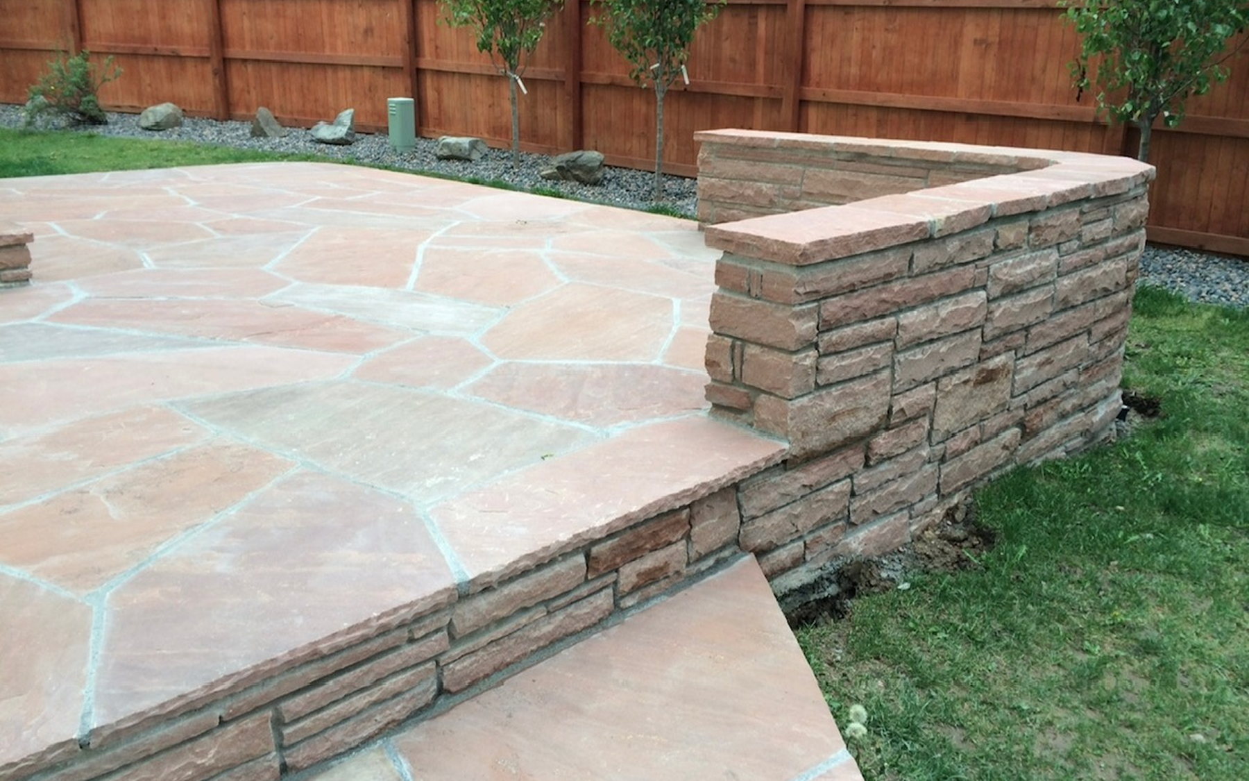 A flagstone patio with a stacked-stone seat wall built by Denka Landscaping